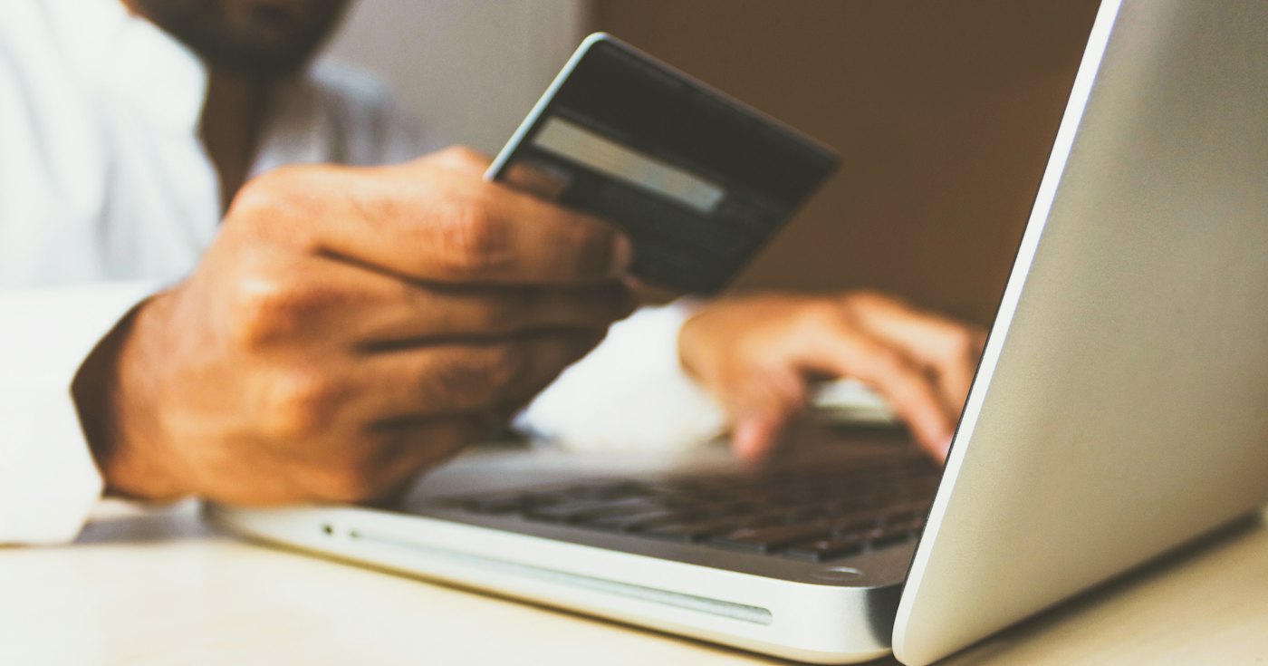 A person holding a credit card in front of a laptop