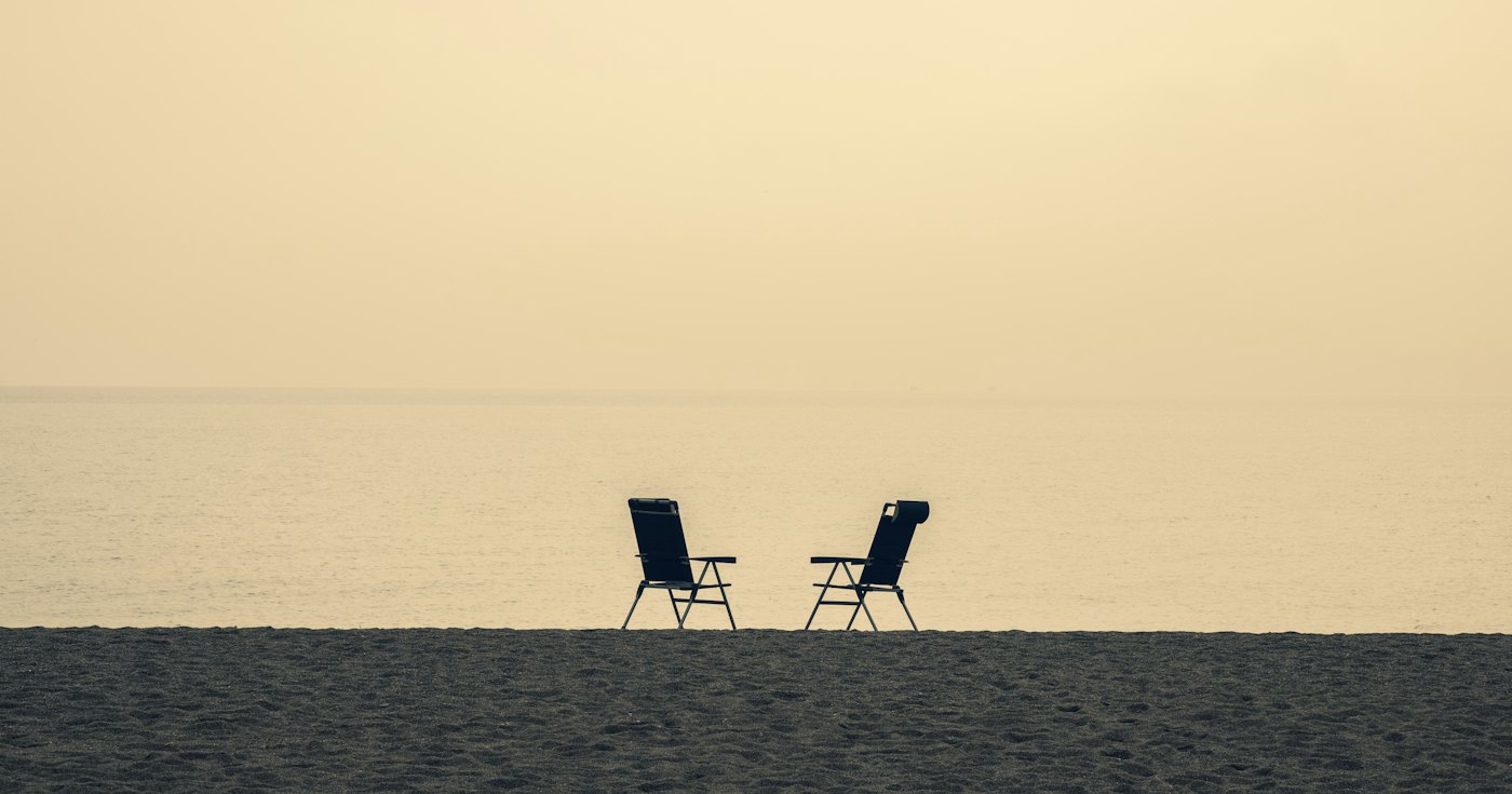 Two folding chairs set apart on a beach