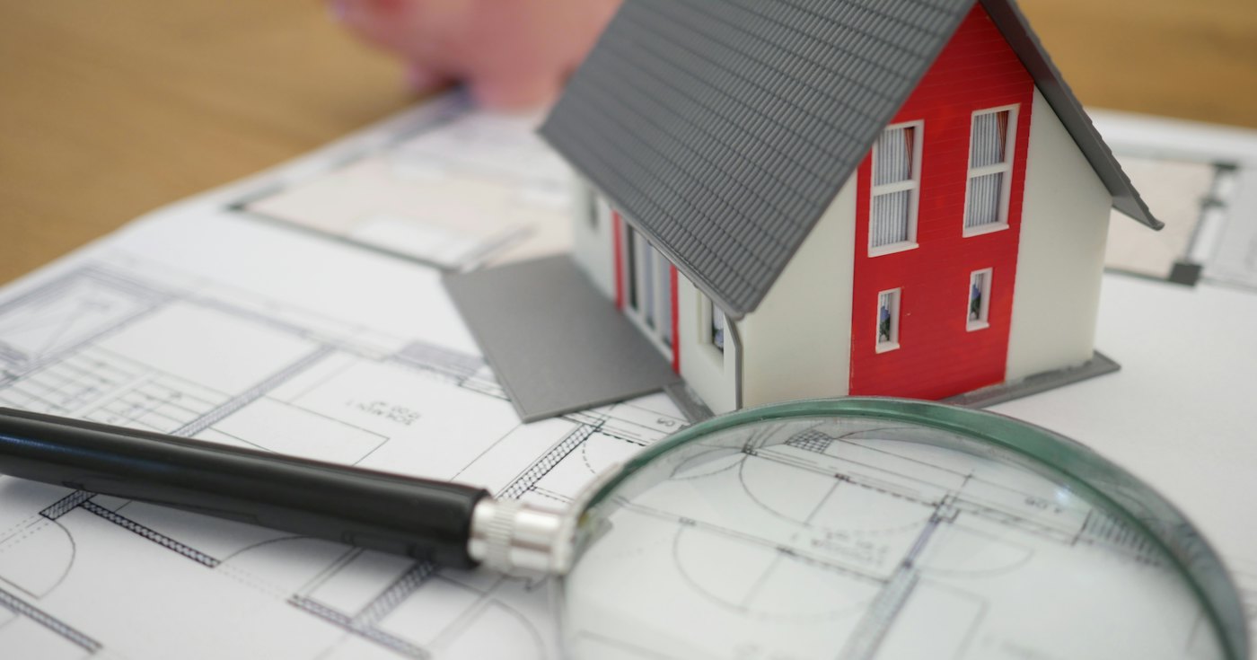 Model house next to a magnifying glass on a desk
