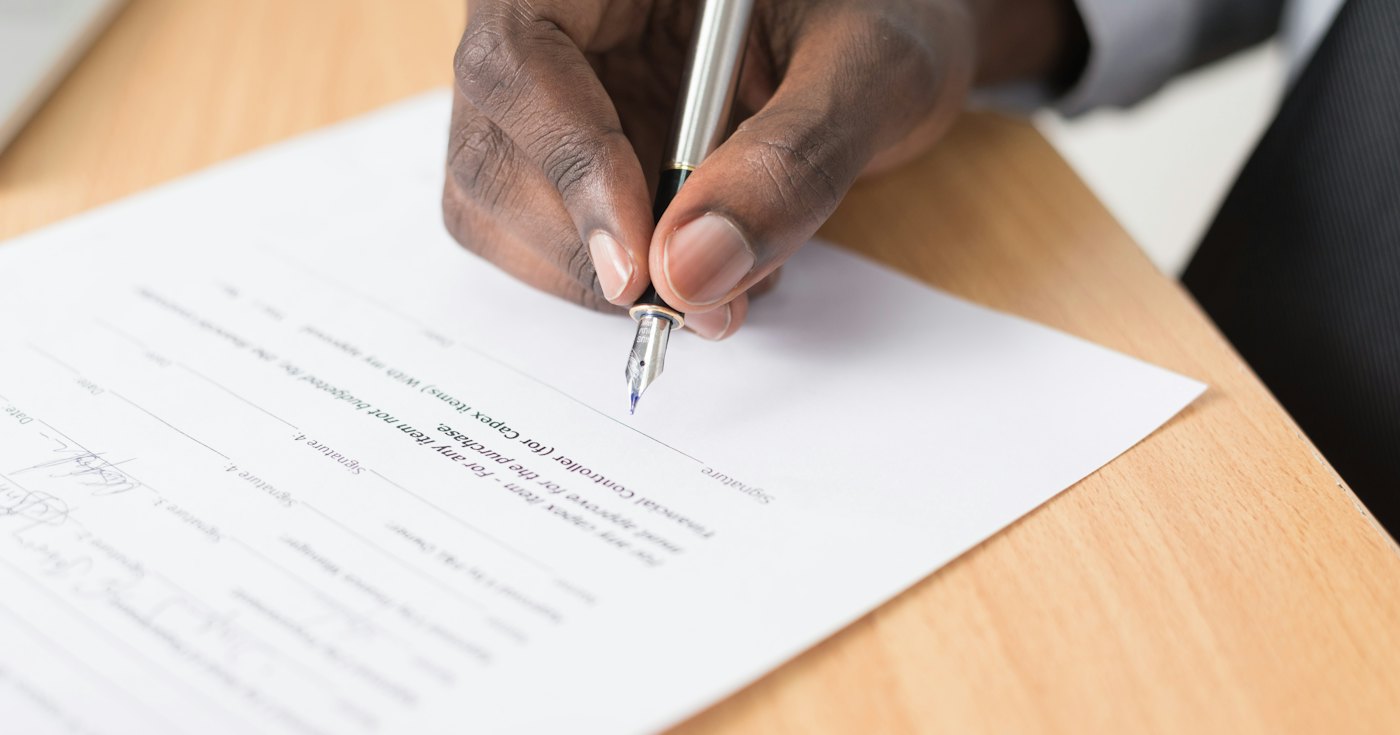 A person signing a document with a pen