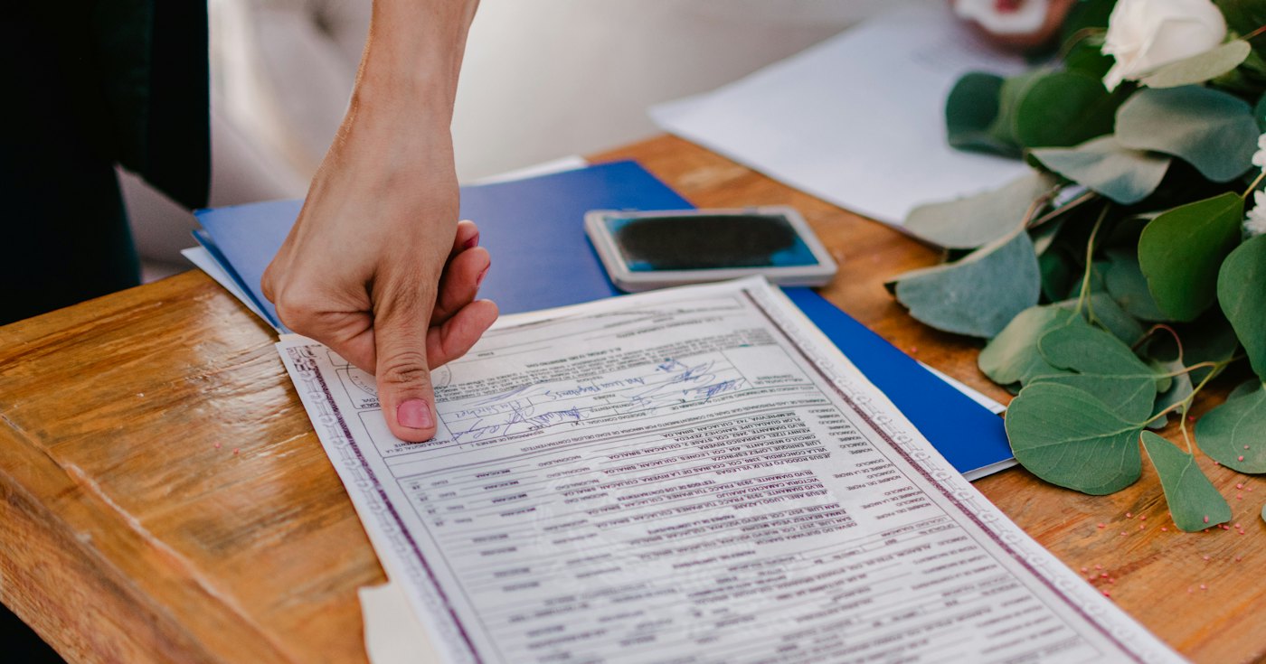 A person pointing at a marriage certificate on a table